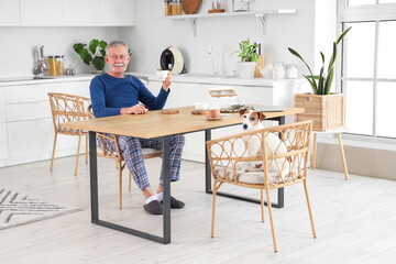 Mature man with cute Jack Russell terrier having breakfast at table in kitchen