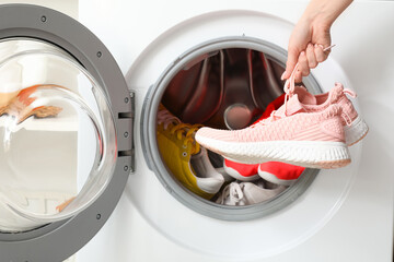 Female hands with sneakers and open washing machine, closeup