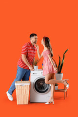 Happy young couple near washing machine on orange background