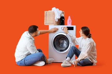 Young couple doing laundry on orange background