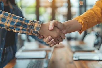 Obraz premium Two people shaking hands in front of a laptop computer