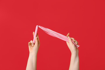 Female hands with whip from sex shop on red background, closeup