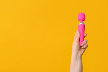 Female hand with pink vibrator on yellow background, closeup