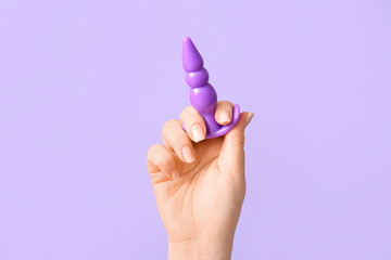 Female hand with anal plug on lilac background, closeup