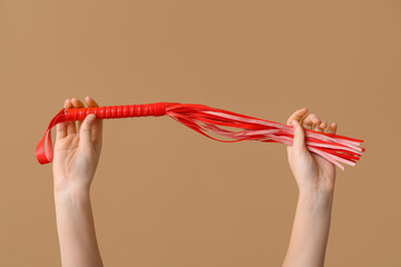 Female hands with whip from sex shop on color background, closeup