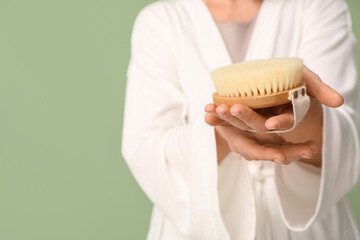 Young woman with body massage brush on green background