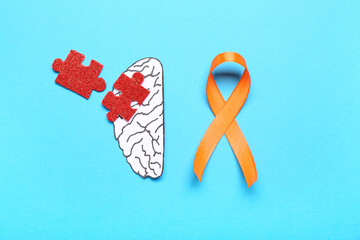 Paper brain with puzzle pieces and orange ribbon on blue background. Multiple Sclerosis Awareness...