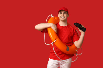 Male lifeguard with ring buoy and binoculars on red background