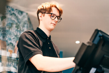 Young waiter serving customer at cash point in cafe. Man working with POS terminal. Cashier,...