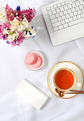 Modern feminine desk, home office. Computer, hyacinth flowers and a cup of tea, macaroons on a sunny table with long shadows, lifestyle concept, comfortable work from home, template for design, 