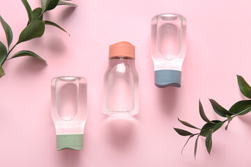 Bottles of clean water and leaves on pink background