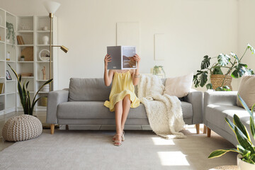 Young pretty woman reading magazine and sitting on sofa in living room