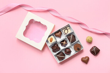 Box with delicious chocolate candies and ribbon on pink background