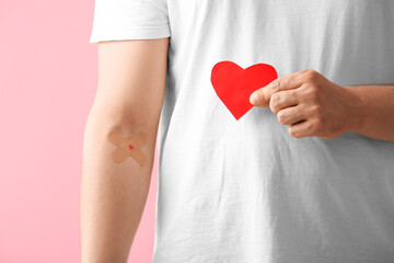 Blood donor with applied medical patches and paper heart on pink background, closeup