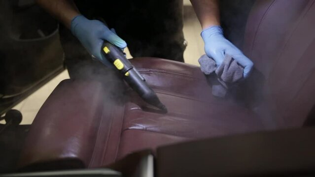 The detailing master cleans the car interior with a hot steam cleaner close-up. Car detailing and the concept of car interior care. Dry cleaning of the car interior, close-up, selective focus.