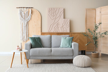 Interior of light living room with grey sofa, olive tree, chest of drawers and coffee table