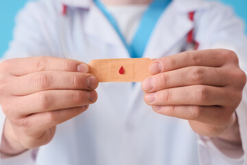 Male doctor with patch on blue background, closeup. Blood donation concept