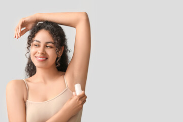 Beautiful young African-American woman applying deodorant on grey background