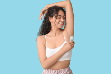 Happy young African-American woman applying deodorant on blue background