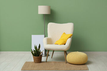 Armchair with cushion, pouf and plant near green wall