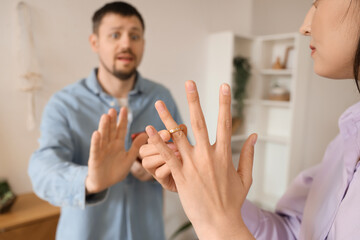 Young woman taking her wedding ring off finger and husband at home, closeup. Cheating concept