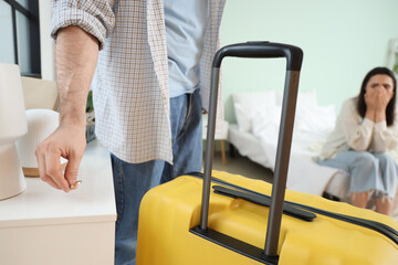 Young man with suitcase putting his wedding ring on shelf in bedroom, closeup. Cheating concept