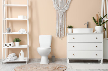 Interior of restroom with toilet bowl and furniture near beige wall