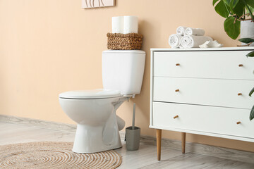 Interior of restroom with toilet bowl and chest of drawers near beige wall