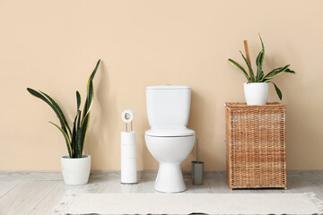 Interior of restroom with toilet bowl, basket and plants near beige wall