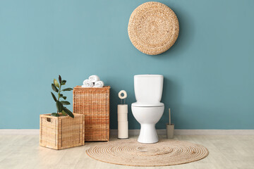 Interior of restroom with toilet bowl plant and basket near blue wall