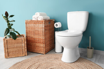 Interior of restroom with toilet bowl plant and basket near blue wall