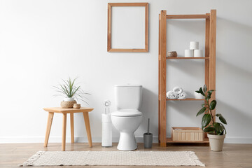 Interior of restroom with toilet bowl, coffee table and shelving unit near white wall