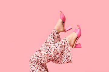 Legs of young woman in trousers and pink open-toed high heels on pink background