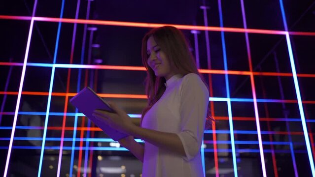 Portrait of Asian Vietnamese woman with Vietnam dress using a tablet device. Colorful neon stripes in night pub in Hanoi. People lifestyle.