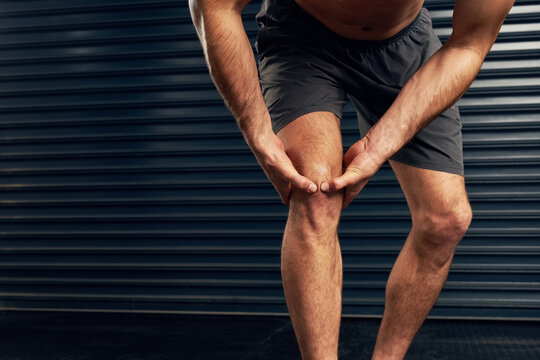 Injured, man or athlete holding knee against dark background for pain, accident or sports emergency. Training, male person and acl tear for leg strength, health and fitness or joint inflammation