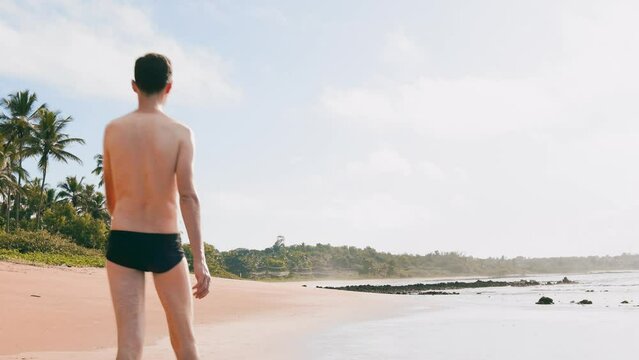 Man walking on the beach sand, wearing a swimwear. Enjoying the summer through outdoor activities at the beach