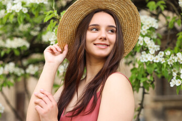 Beautiful woman in straw hat near blossoming tree on spring day