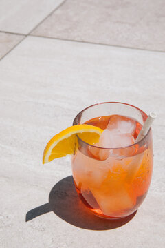 A glass of iced aperol spritz garnished with an orange and a compostable paper straw outside.