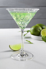 Delicious Margarita cocktail with ice cubes in glass and lime on white table