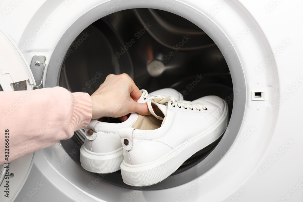 Wall mural Woman putting stylish sneakers into washing machine, closeup