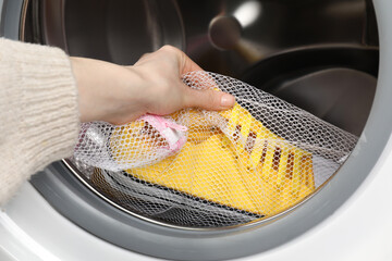 Woman putting stylish sneakers into washing machine, closeup