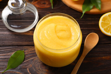 Delicious lemon curd in glass jar, fresh citrus fruit and spoon on wooden table