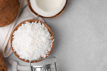 Coconut flakes in bowl, nuts and grater on light grey table, top view. Space for text