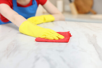 Woman cleaning white marble table with rag in kitchen, closeup