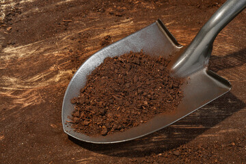 Metal shovel with fertile soil on dirty wooden surface