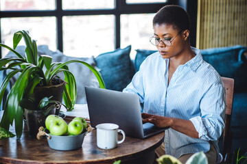 Young attractive African American woman nutritionist is working on laptop in a beautiful green...