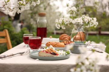 Stylish table setting with beautiful spring flowers, fruit drink and pie in garden