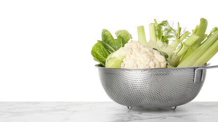 Metal colander with different vegetables on marble table against white background, space for text