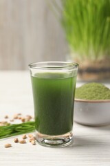 Wheat grass drink in shot glass on white wooden table, closeup