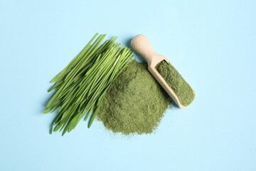Pile of wheat grass powder, scoop and fresh sprouts on light blue table, flat lay